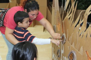 A woman and child touch a large cardboard prop.