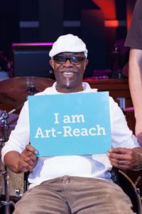 A man holds up a sign that reads "I am Art Reach" at a Live Connections concert.