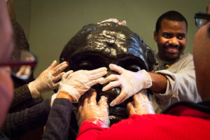 A group of people touch a statue with gloves on during a touch tour at the Rodin Museum.