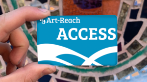 a hand holds a Blue and White card that reads Art-Reach ACCESS with swirl logo.. behind the card is a blury mosaic wall
